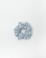 A single light blue satin scrunchie centered on a clean white background.