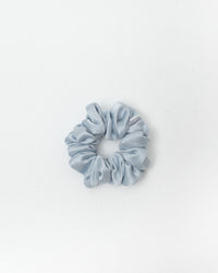 A single light blue satin scrunchie centered on a clean white background.