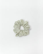 A single fabric scrunchie in a muted sage green color, photographed flat against a clean white background.