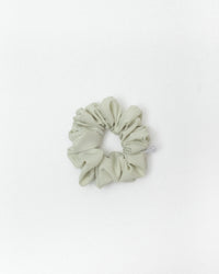 A single fabric scrunchie in a muted sage green color, photographed flat against a clean white background.