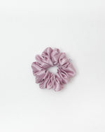 A single dusty pink satin scrunchie centered on a clean white background.