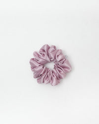 A single dusty pink satin scrunchie centered on a clean white background.