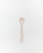 A small ceramic spoon in a pale pink color with subtle star details, centered on a plain white background.