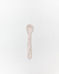 A small ceramic spoon in a pale pink color with subtle star details, centered on a plain white background.