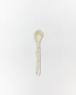 A small handmade ceramic spoon in a pale sage green glaze, centered on a plain white background.