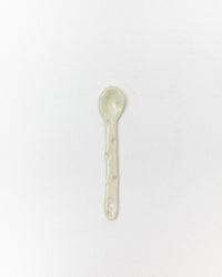 A small handmade ceramic spoon in a pale sage green glaze, centered on a plain white background.