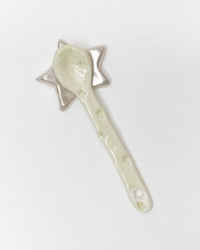 A ceramic spoon with a star-shaped handle, decorated with a pale green glaze and small star motifs, set against a plain white background.