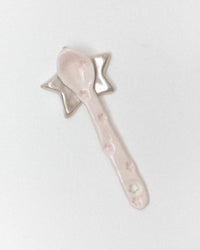 A light pink ceramic spoon with a star-shaped handle, photographed on a plain light gray background.