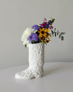 White textured boot-shaped vase with colorful flowers on a light gray background
