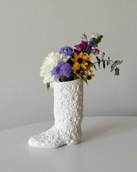 White textured boot-shaped vase with colorful flowers on a light gray background
