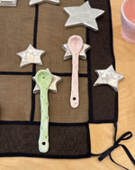 Decorative spoons and star-shaped objects on a black cloth with a pink cup in the corner.