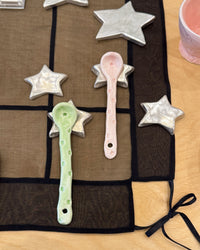 Decorative spoons and star-shaped objects on a black cloth with a pink cup in the corner.