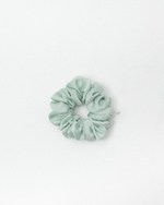 A gif of photos showcasing 7 scrunchies in muted pastel and earthy colors, including dusty blue, pink, sage green, melon green, cream, burgundy, and dusty blue set against a plain white background.